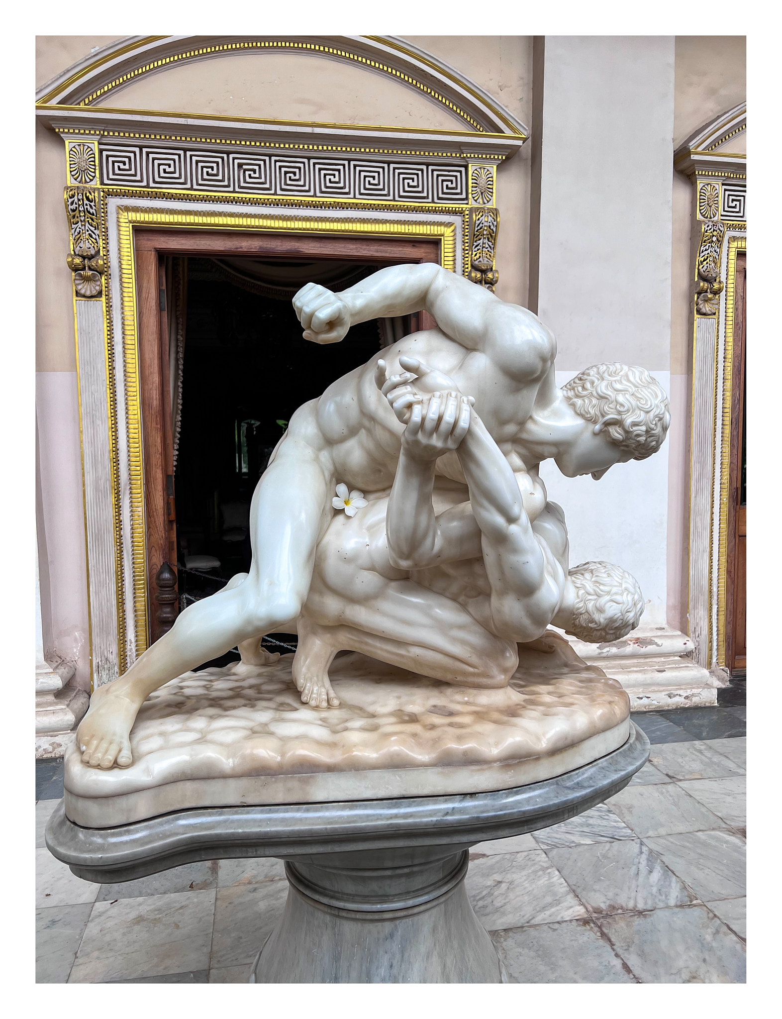 A Greek marble sculpture of two men fighting, a flower has been place by someone of the man's private area