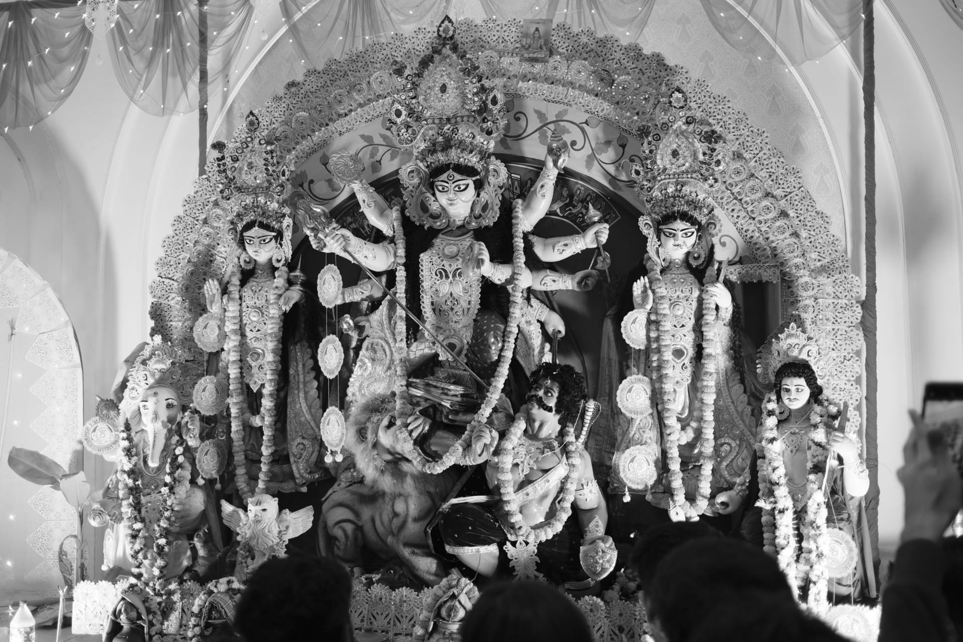 Black and white photo of the Durga idol at a pandal, with Lakshmi, Saraswati, Ganesha and Kartikeya around her and Mahishasura at her feet
